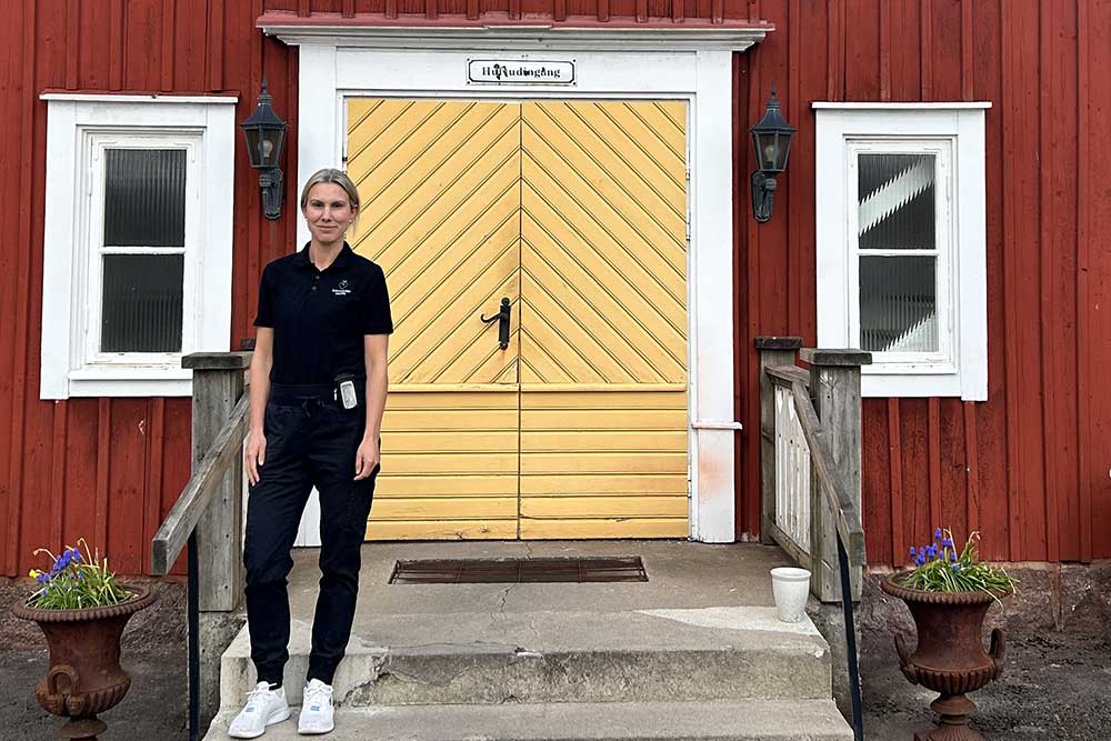 Karin Råberg utanför ett rött hus med gul dörr