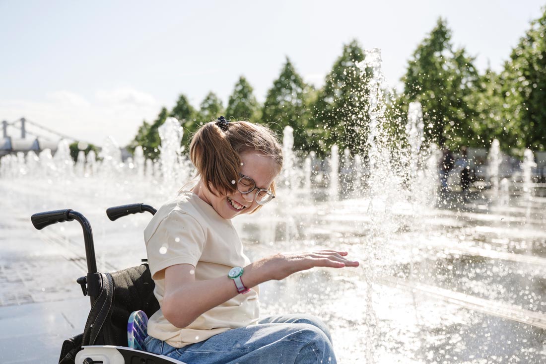 Flicka i rullstol leker i fontän